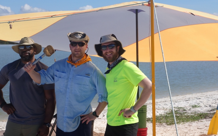 three people smile at the camera while standing under a shelter on a beach